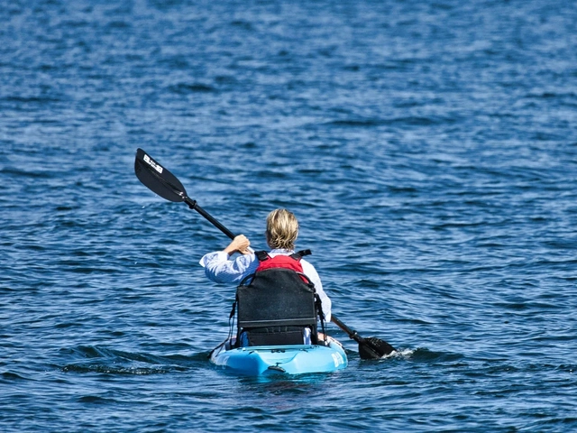 Man kayaking on a lake with brilliant blue water in a blue kayak.