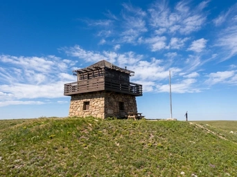 The Cement Ridge Fire Lookout stone building on a hill with scattered clouds. Located in Beulah Wyoming, Black Hills.