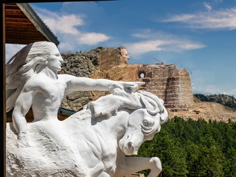 The statue of Crazy Horse with the mountain carving in the background - Black Hills also visible.