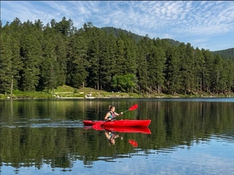 Woman kayaking on Sheridan Lake in the Black Hills. Pine trees in the background, reflection on the water.